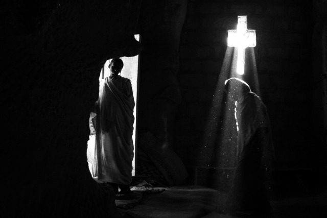 Light catches a crucifix in a church in Lalibela, as an Ethiopian pilgrim stands at the entrance. Photo by Gali Tibbon